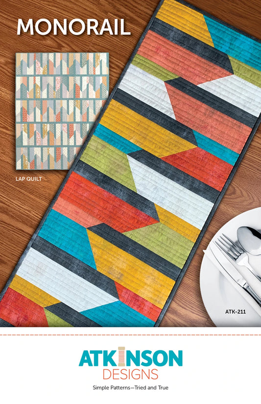 Colorful quilt with geometric pattern on a wooden surface, featuring Atkinson Designs branding.