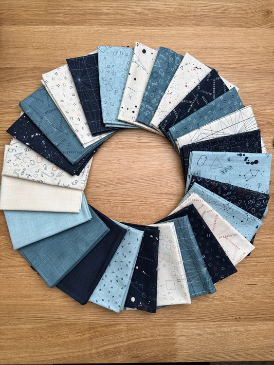 A circular arrangement of Data by Janet Clare fabric swatches in various shades of blue, navy, cream, and white with celestial and geometric patterns, displayed on a light brown wooden surface.