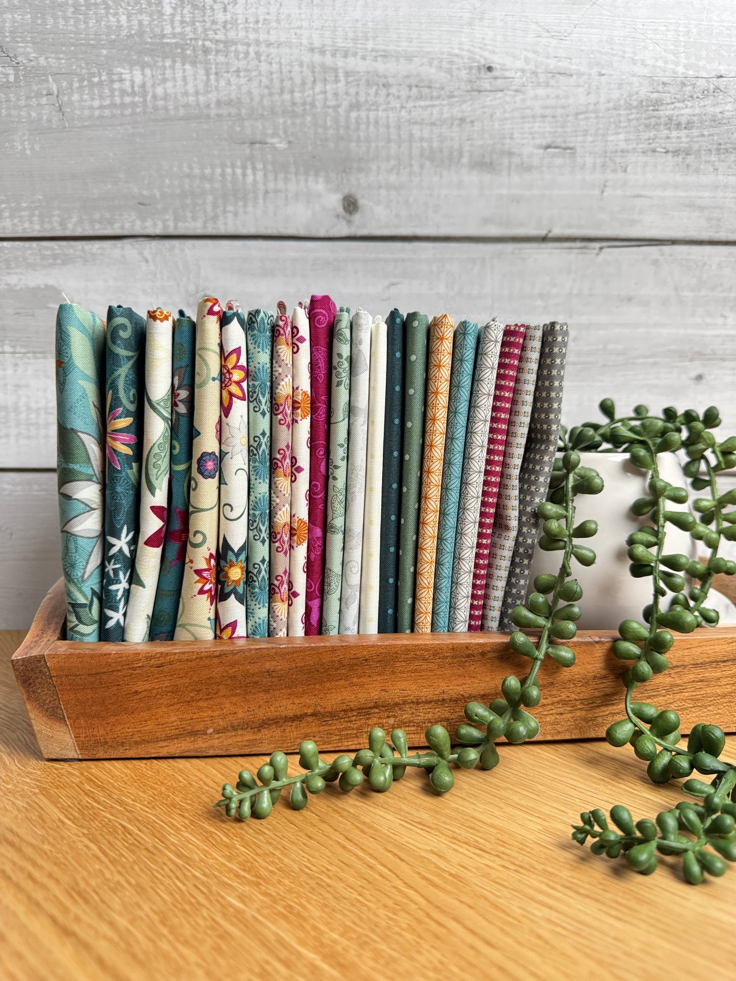 Where the Wild Flowers Are fat quarter bundle standing on end on a wooden tray next to a plant, shop-cut by Treeline Quilting