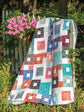 Colorful quilt draped over a wooden post with pink flowers and greenery in the background
