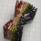 A bundle of folded After the Bloom patterned fabric pieces tied with a white string, displayed on a white gridded cutting mat. The fabrics feature various floral and botanical designs in rust red, dusty pink, olive green, mustard yellow, and navy blue.