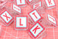 Clear plastic alphabet letter stamps with red and light blue scalloped borders and white letter faces, scattered on a pink cutting mat.