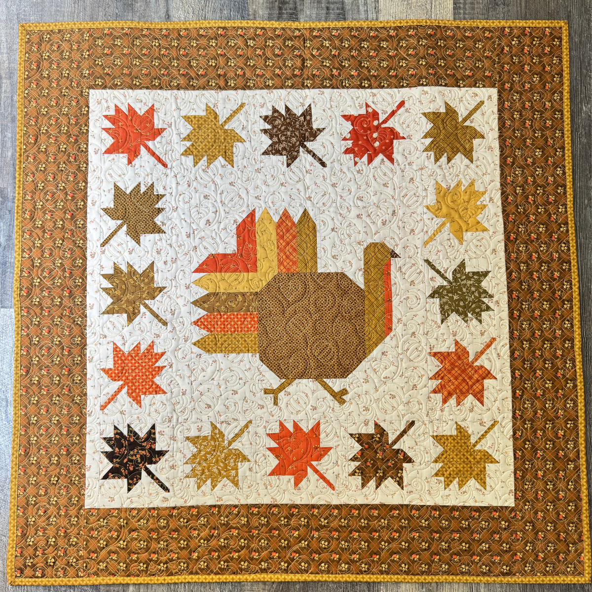 Autumn Hues completed quilt featuring a turkey in the center, surrounded by fall colored leaves and a wide border.  Made using the Bountiful fabric collection by Sandy Gervais