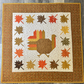 Autumn Hues completed quilt featuring a turkey in the center, surrounded by fall colored leaves and a wide border.  Made using the Bountiful fabric collection by Sandy Gervais