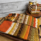 27 piece Bountiful fat quarter bundle spread out on a tray with a stacked complete fat quarter bundle behind. 