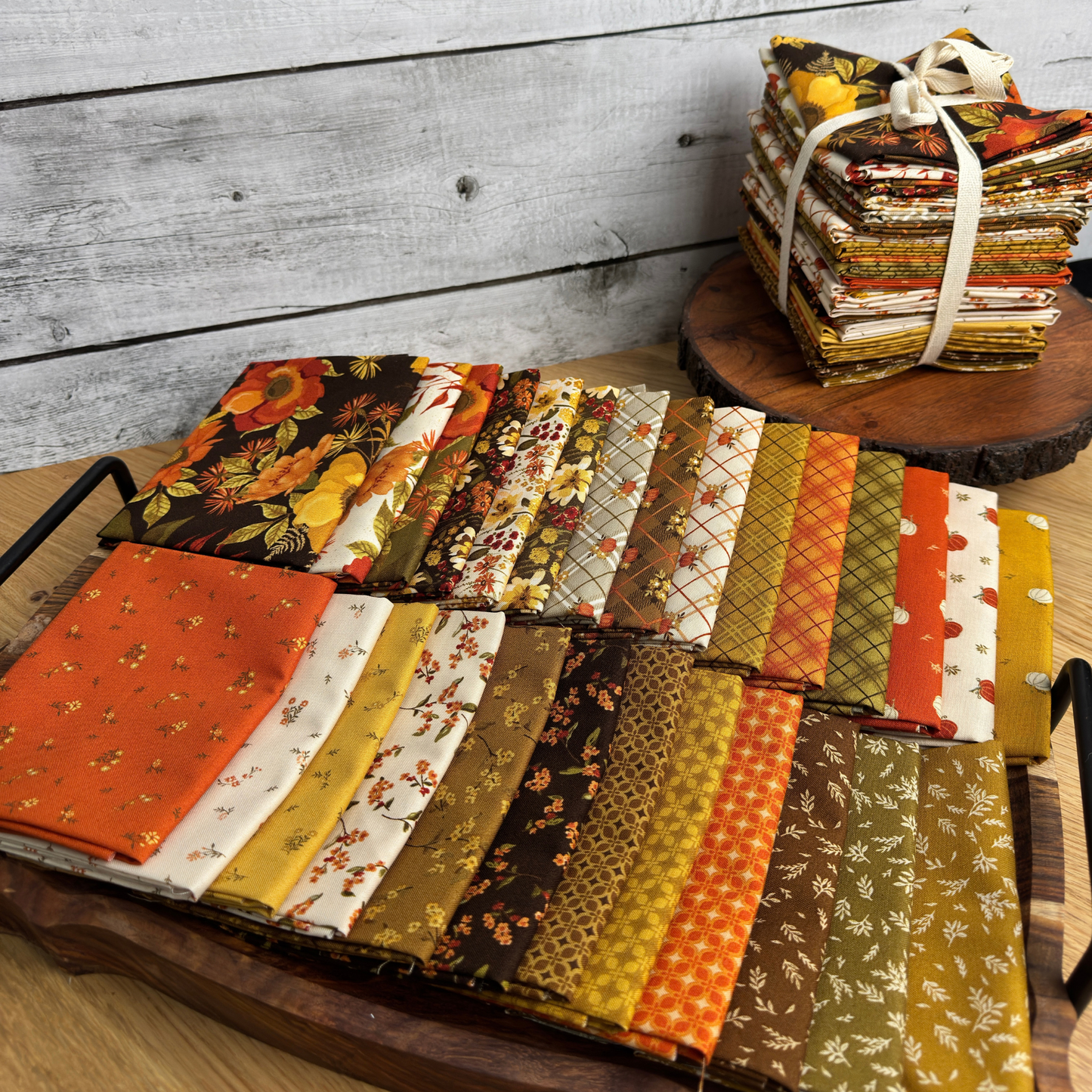 27 piece Bountiful fat quarter bundle spread out on a tray with a stacked complete fat quarter bundle behind. 