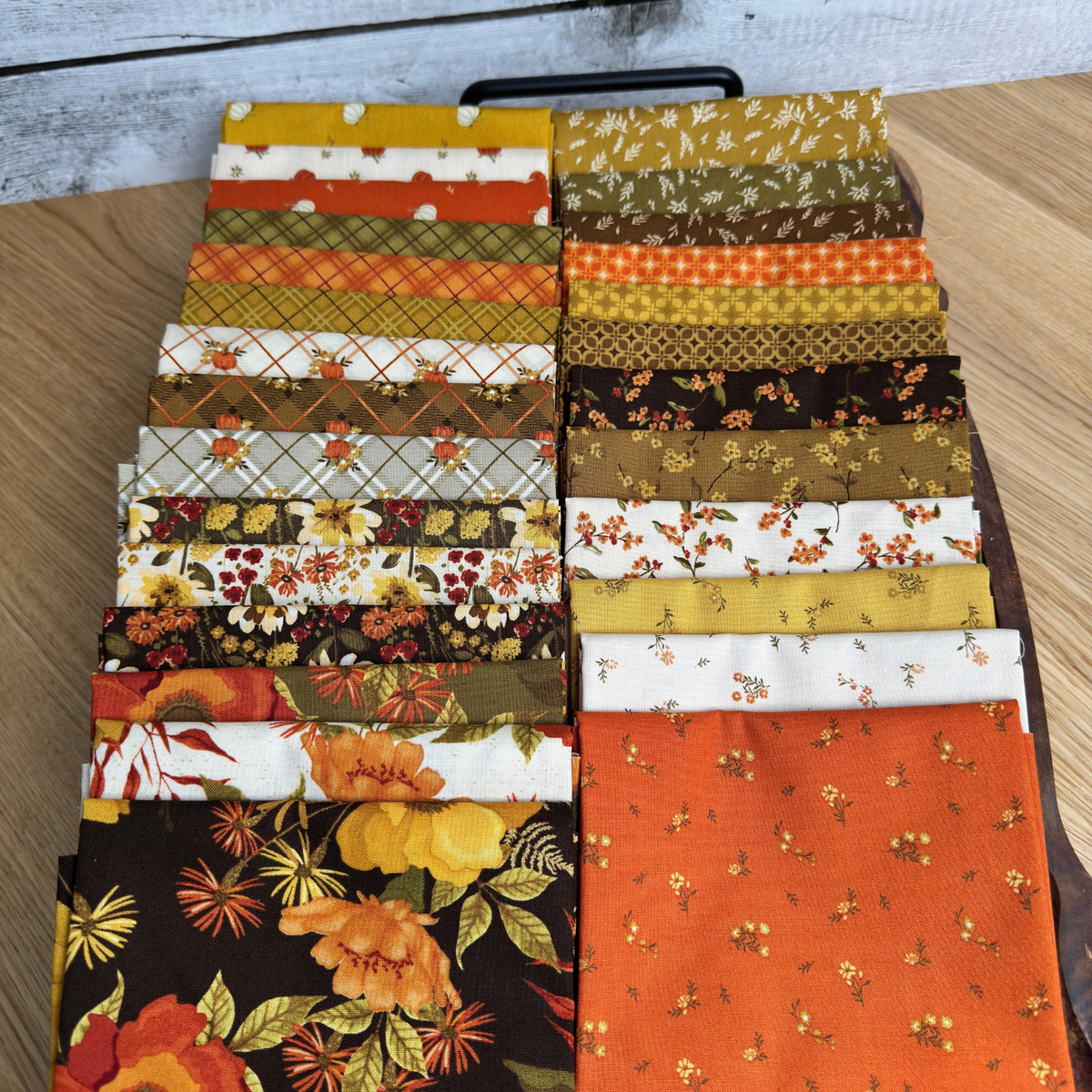 Bountiful fabric collection fall colors with leaf, floral, and pumpkin prints spread out on a tray. 