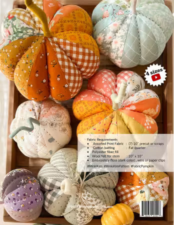 A collection of handmade fabric pumpkins in various colors and patterns, arranged inside a wooden box. The pumpkins feature different prints like gingham, floral, and polka dots in shades of orange, yellow, green, pink, and purple.