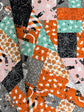 A close-up of a quilted fabric featuring a patchwork design of various Halloween-themed prints, including orange pumpkins, white ghosts, black spiderwebs, and pink haunted houses.
