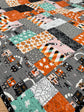 A close-up of a patchwork quilt featuring various Halloween-themed fabric prints, including orange pumpkins, black spiderwebs, pink ghosts, and gray haunted houses.