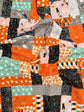 A close-up of a patchwork quilt featuring Halloween-themed fabrics with orange, black, pink, gray, and mint green patterns of pumpkins, ghosts, spiderwebs, and haunted houses.