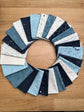 A circular arrangement of Data by Janet Clare fabric swatches in various shades of blue, navy, cream, and white with celestial and geometric patterns, displayed on a light brown wooden surface.