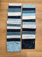 Two vertical stacks of Data fabric swatches by Janet Clare in shades of blue, navy, white, and gray with various printed patterns, arranged on a wooden surface.