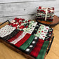 Stylized photo of Evergreen Wishes Fat quarters in a stack behind a tray of fat quarters spread out to show the Christmas prints