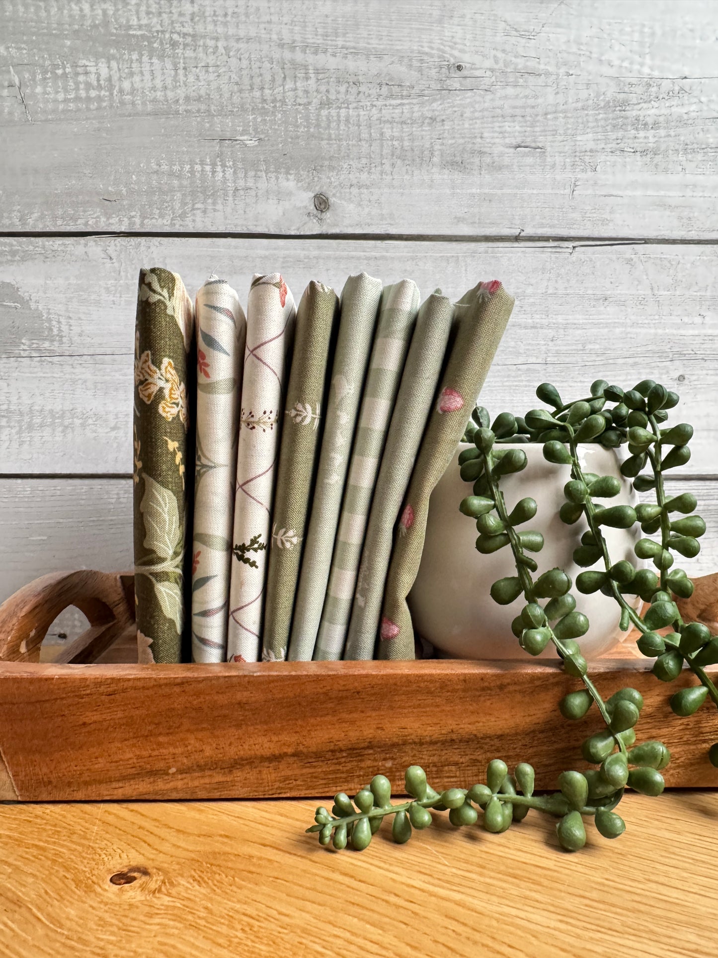 Green Hedgerow Haven petite fat quarter bundle standing on end on a wooden tray next to a plant