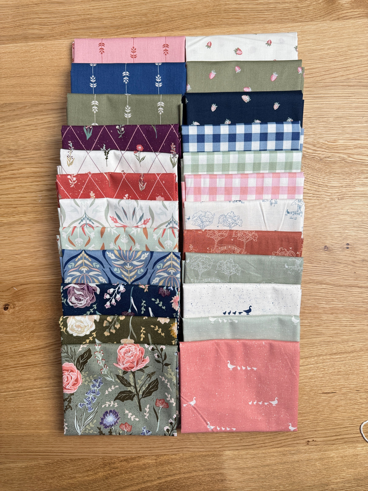 Hedgerow Haven fat quarter bundle standing on end on a wooden tray next to a plant, shop-cut by Treeline Quilting