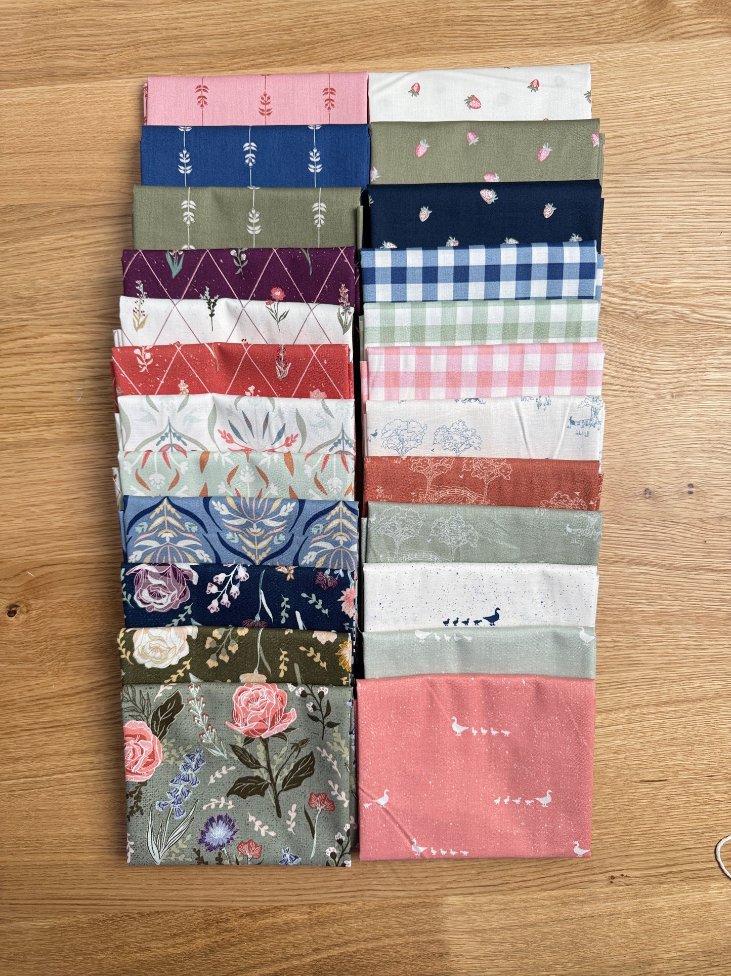 Hedgerow Haven fat quarter bundle standing on end on a wooden tray next to a plant, shop-cut by Treeline Quilting