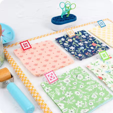 Colorful fabric samples with floral patterns on a white surface, surrounded by sewing tools.