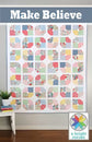 Make Believe quilt pattern cover.  A quilted wall hanging or patchwork textile displayed indoors, featuring a grid of colorful geometric and floral fabric squares on a white base. The top has a blue-gray banner with the text 'Make Believe,' and a 'a bright corner' logo appears in the lower right corner.