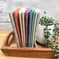 Nine Quiltessential Minis stripe fat quarters standing on end on a tray beside an artificial plant.