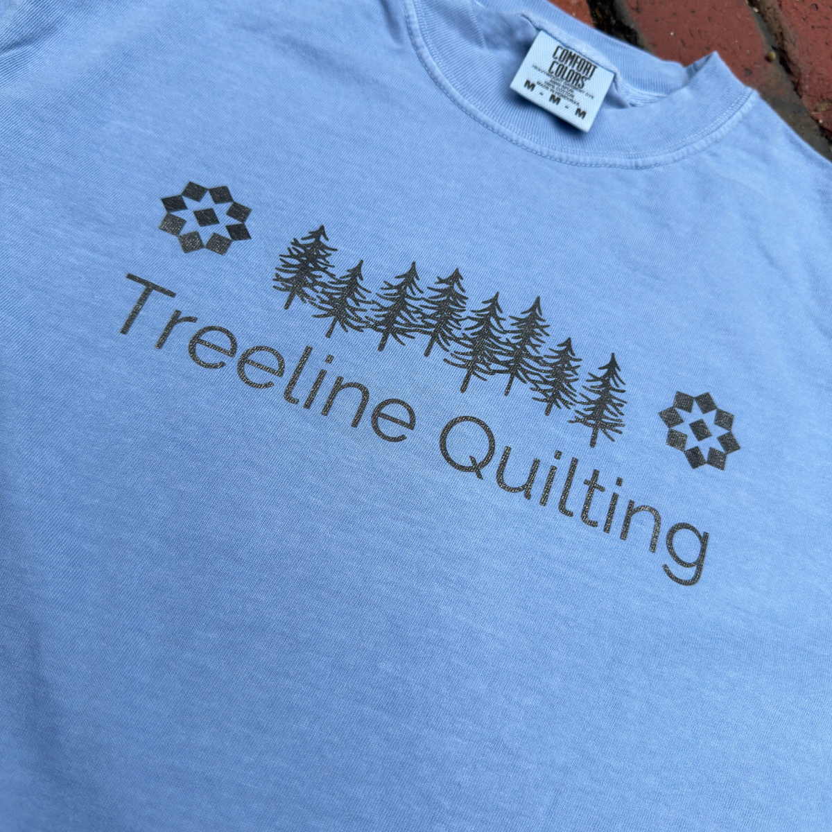 Close up of a Comfort Colors shirt with Treeline Quilting Logo on front