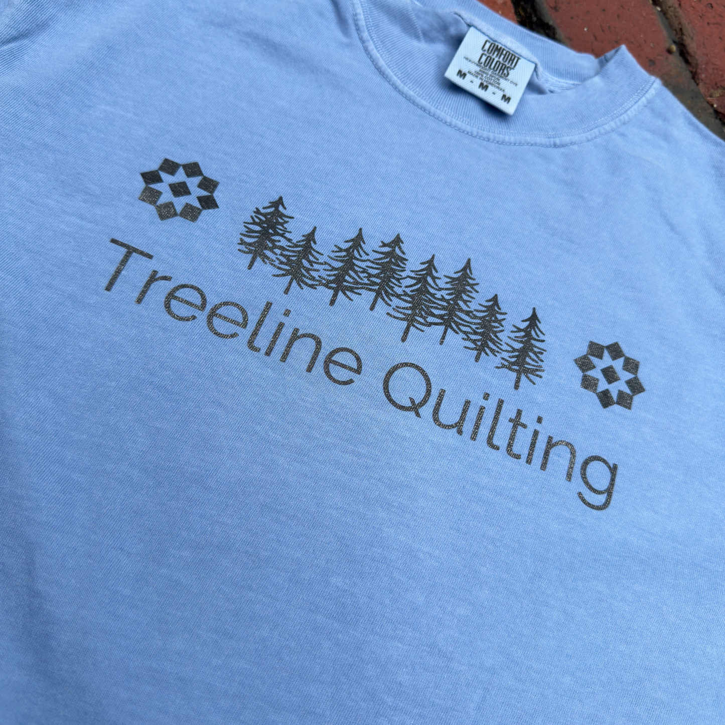 Close up of a Comfort Colors shirt with Treeline Quilting Logo on front