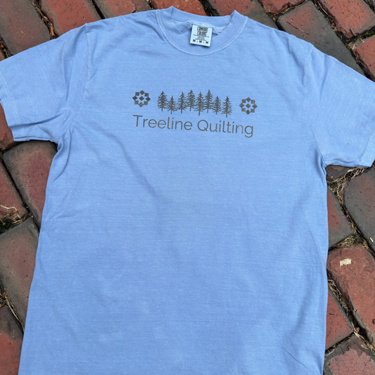 Flat lay of a Comfort Colors shirt with Treeline Quilting Logo on front