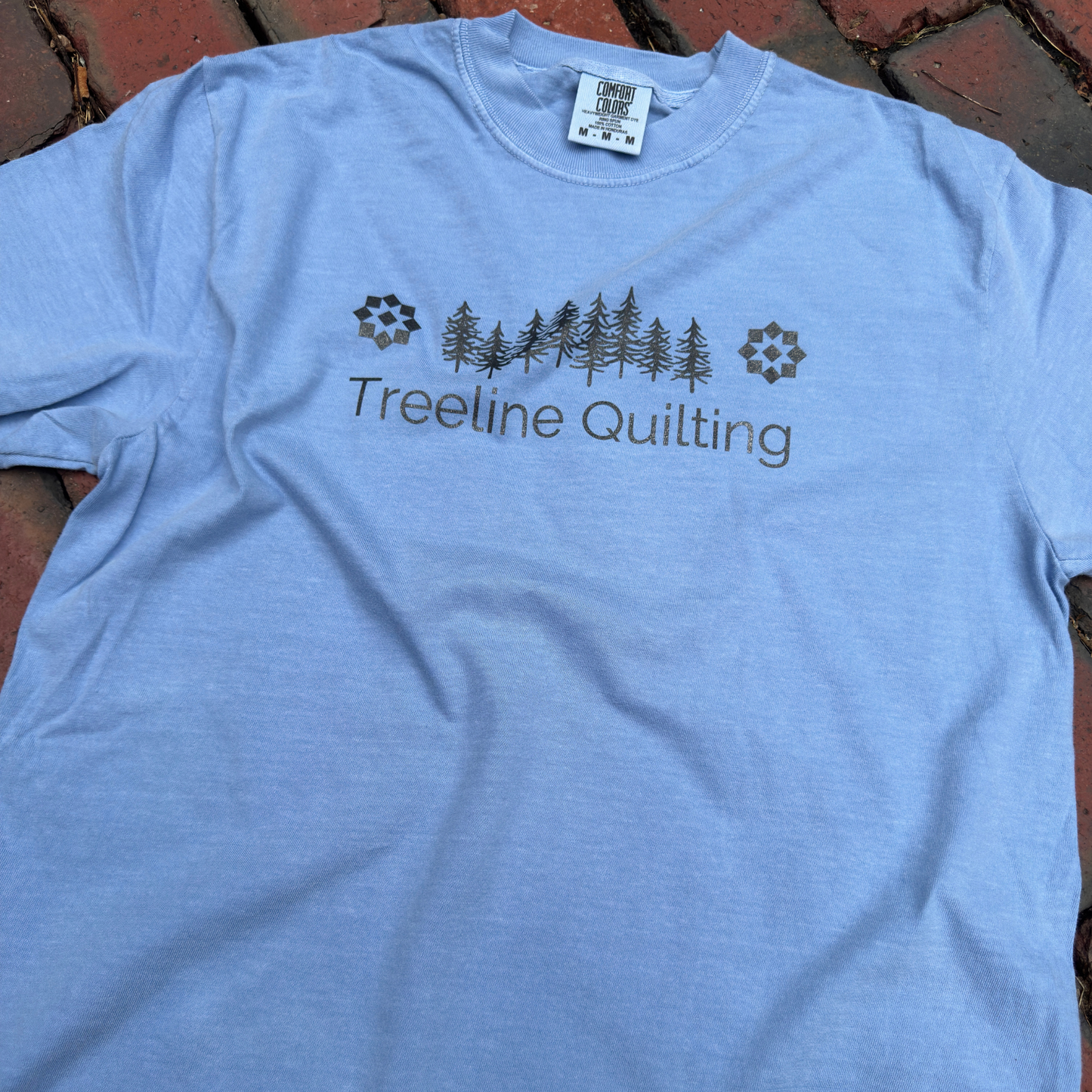 Stylized photo  of a Comfort Colors shirt with Treeline Quilting Logo on front
