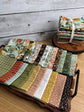 Worth Repeating fat quarters by Sandy Gervais laid out on a tray with a stack of the collection elevated behind. 