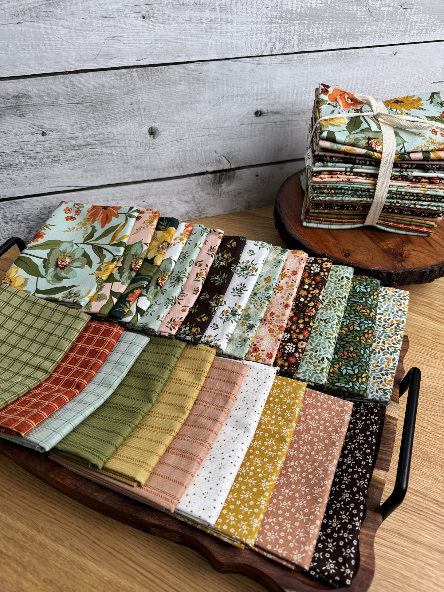 Worth Repeating fat quarters by Sandy Gervais laid out on a tray with a stack of the collection elevated behind. 
